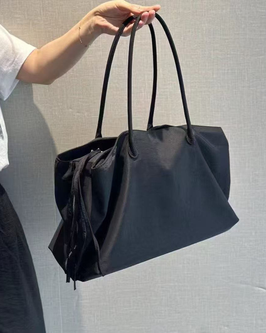 Black handbag held by a person against a gray background
