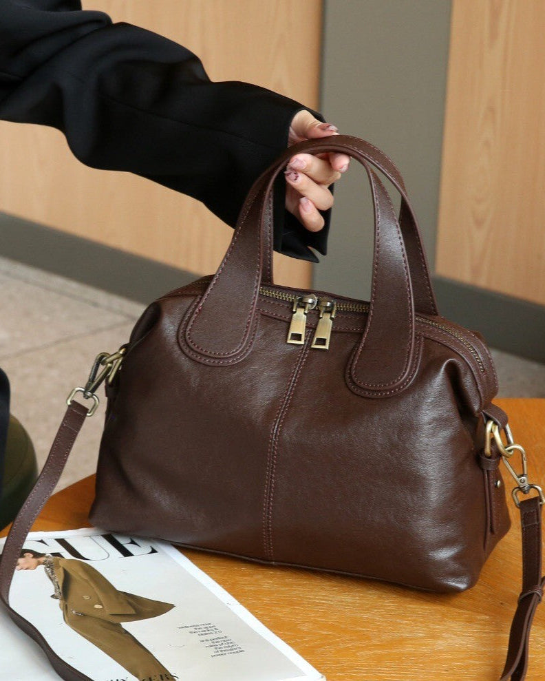 Brown leather handbag on a wooden table with a magazine underneath