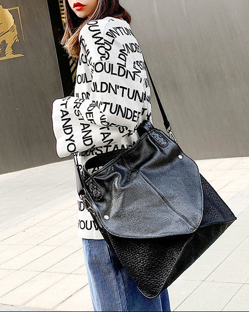 Woman holding a black leather handbag in front of a building entrance.