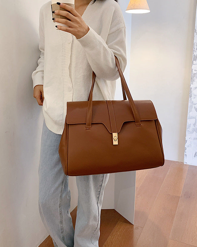 Person holding a brown leather handbag in a minimal indoor setting