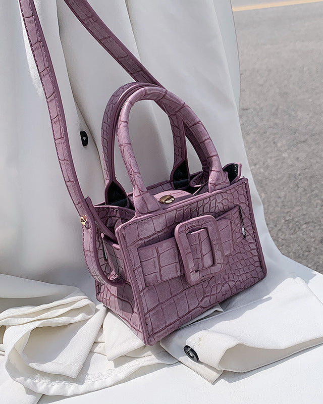 Purple textured handbag on a white surface with a blurred background