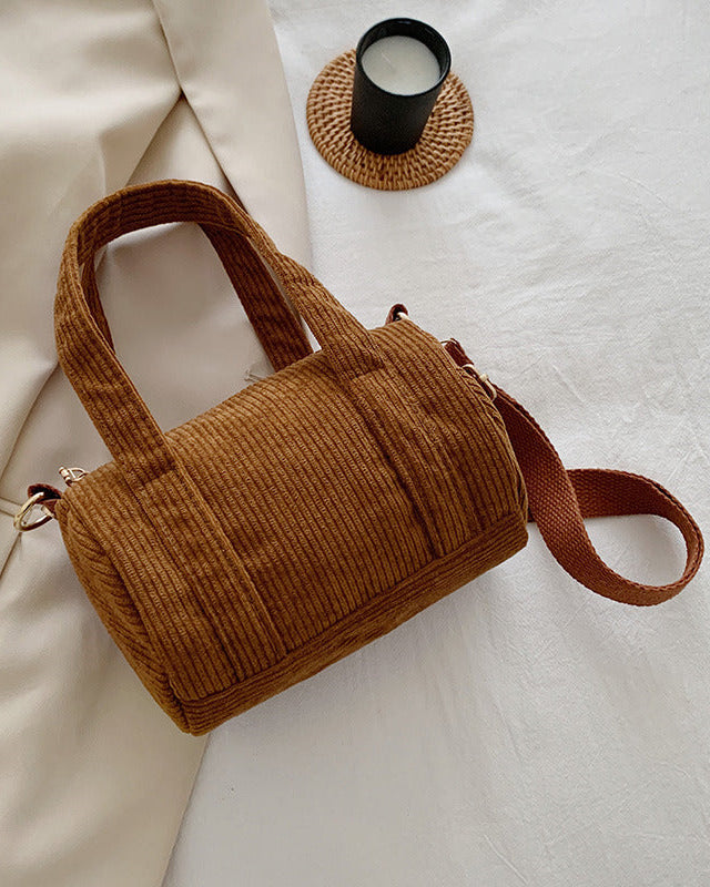 Brown textured handbag on a light surface with a beige fabric and black candle in the background