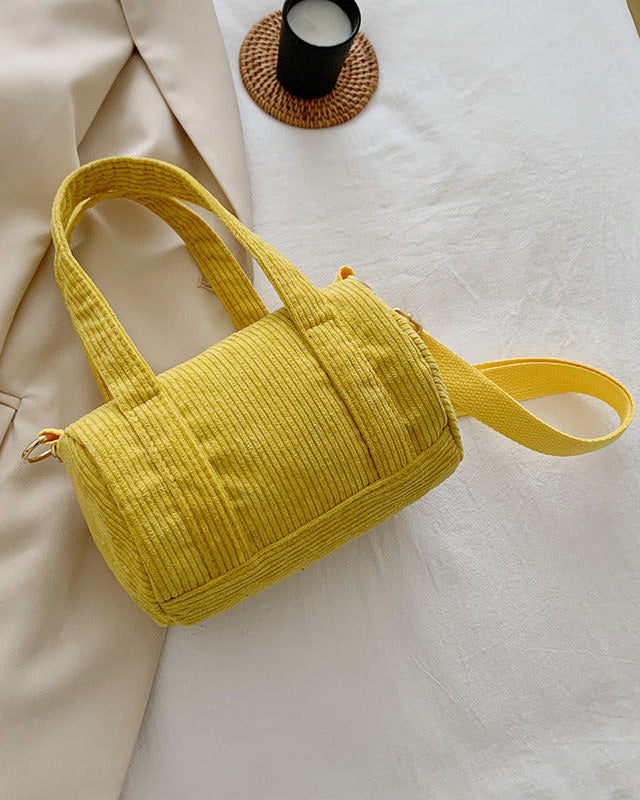 Yellow textured handbag on a light surface with a beige coat and candle in the background