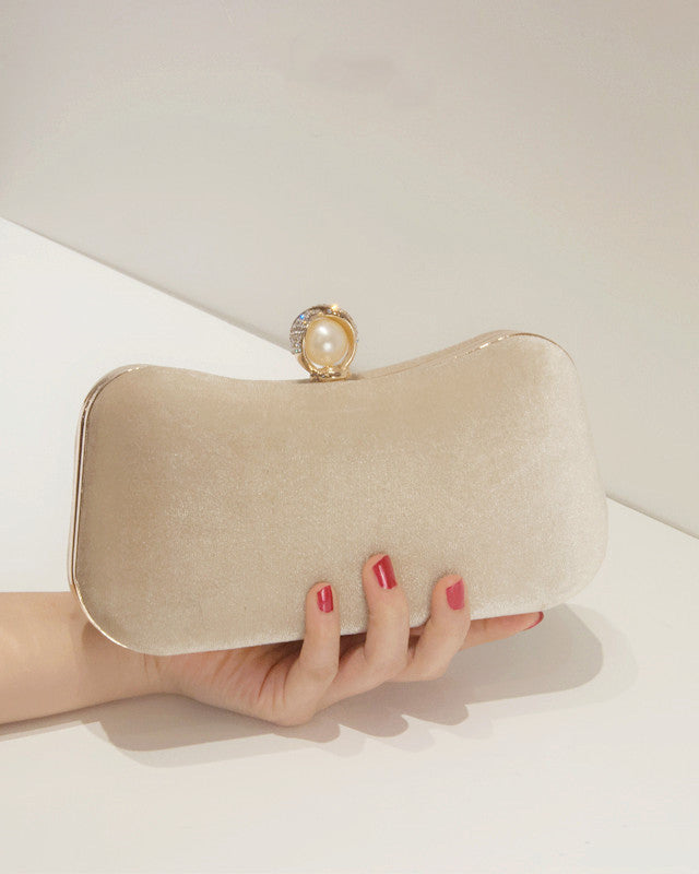 Beige clutch bag with pearl handle held by a hand on a white surface