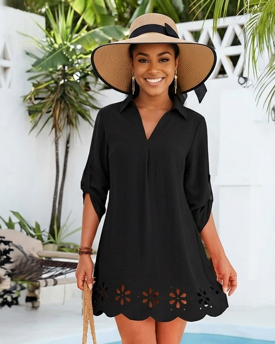 Woman in a black dress with floral details standing by a pool with palm trees in the background