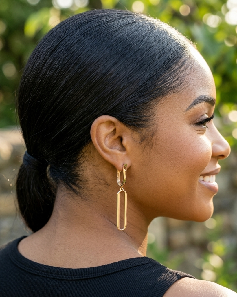 Woman with styled hair and gold earrings against a blurred natural background