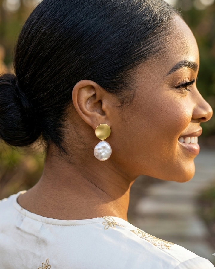Woman wearing gold and pearl earrings with a blurred natural background