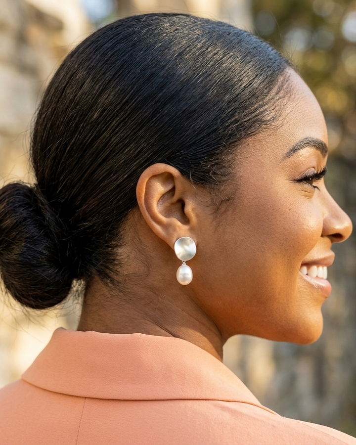 Woman with styled hair and pearl earrings, wearing a peach-colored top.
