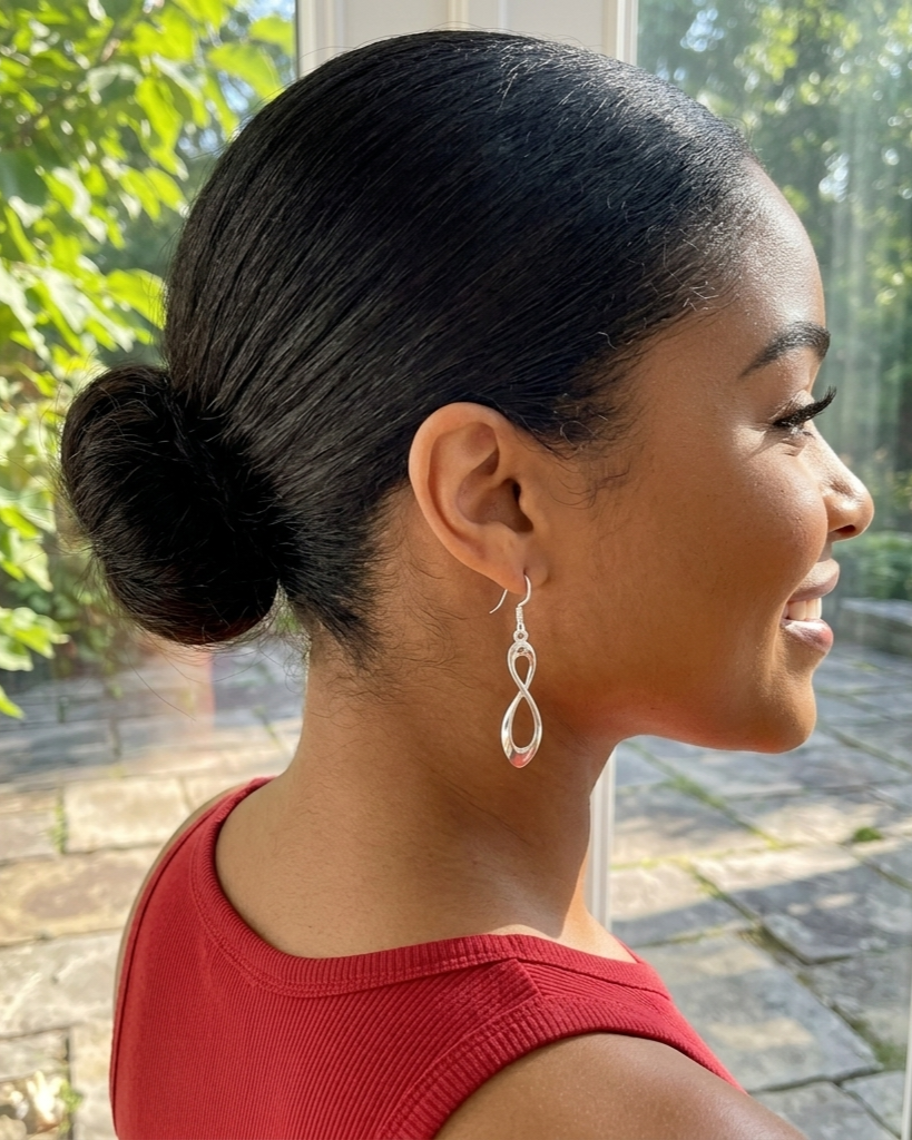 Woman with styled hair and earrings, wearing a red top, outdoors.
