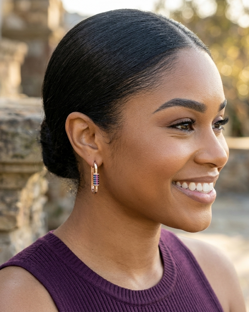 Woman with styled hair and earrings, wearing a purple top, outdoors.