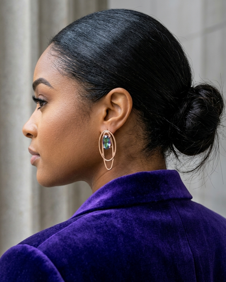 Woman with styled hair wearing a purple coat and colorful earrings.