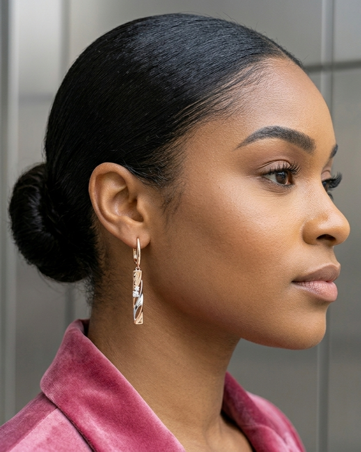 Woman with styled hair wearing a pink garment and gold earrings.