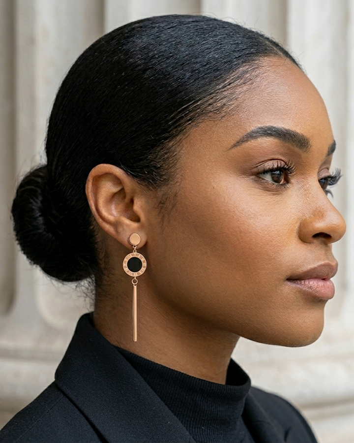 Woman wearing a gold earring with a black stone against a neutral background