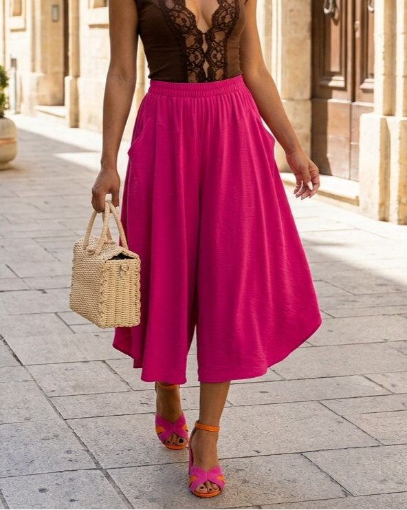 Woman in a pink dress with a black lace top walking down a sunlit street.