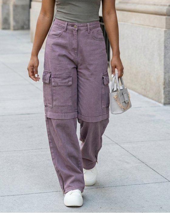 Woman wearing a gray top and purple cargo pants walking on a sidewalk.