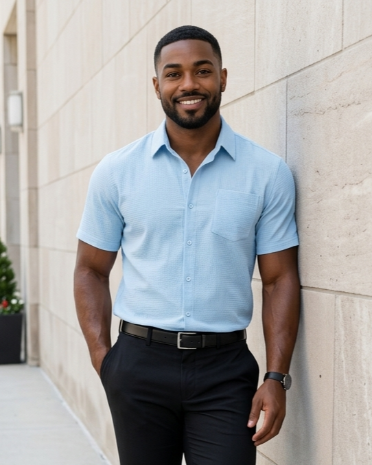 Man in light blue shirt and black pants leaning against a stone wall.