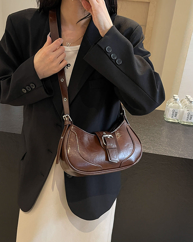Person wearing a black blazer holding a brown leather handbag in an indoor setting.