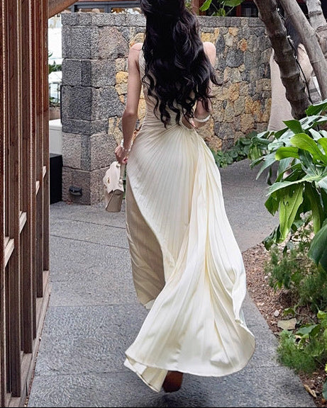 Woman in a white dress walking through a garden with trees and plants.