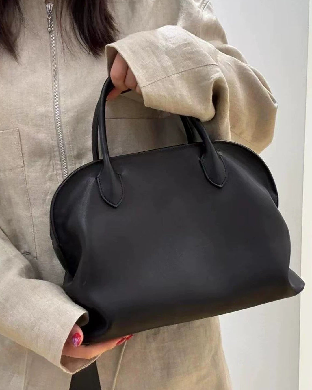 Person holding a black handbag against a neutral background
