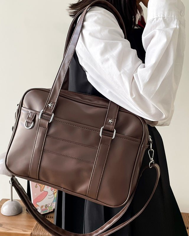 Person wearing a brown leather bag over their shoulder with a neutral background