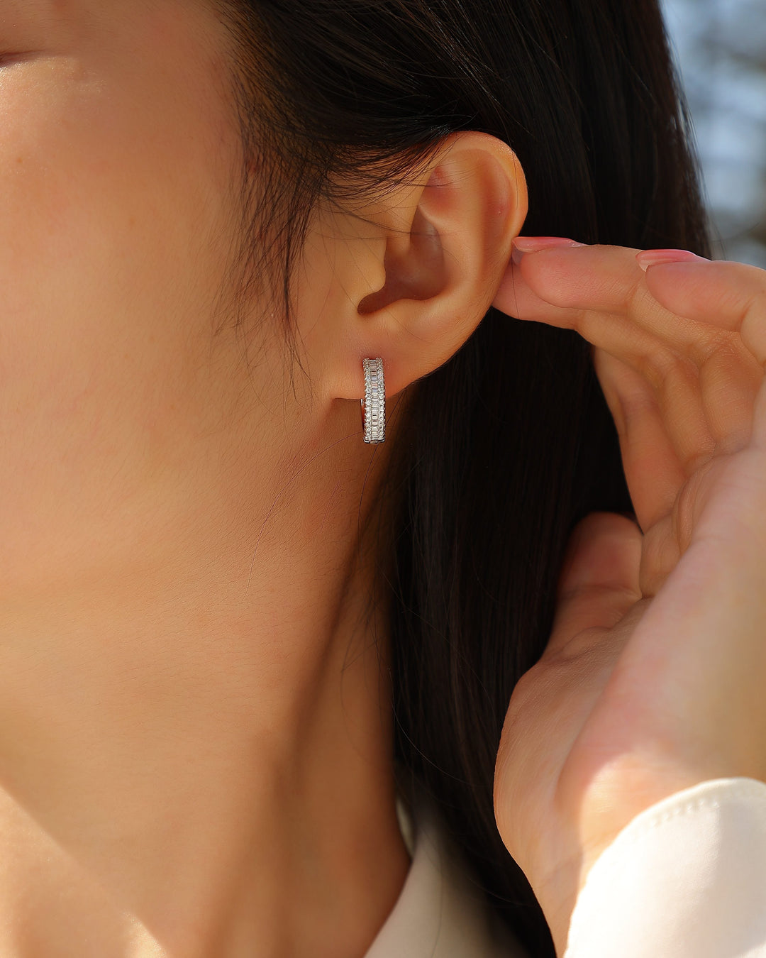 Close-up of a person wearing a silver hoop earring with a blurred background