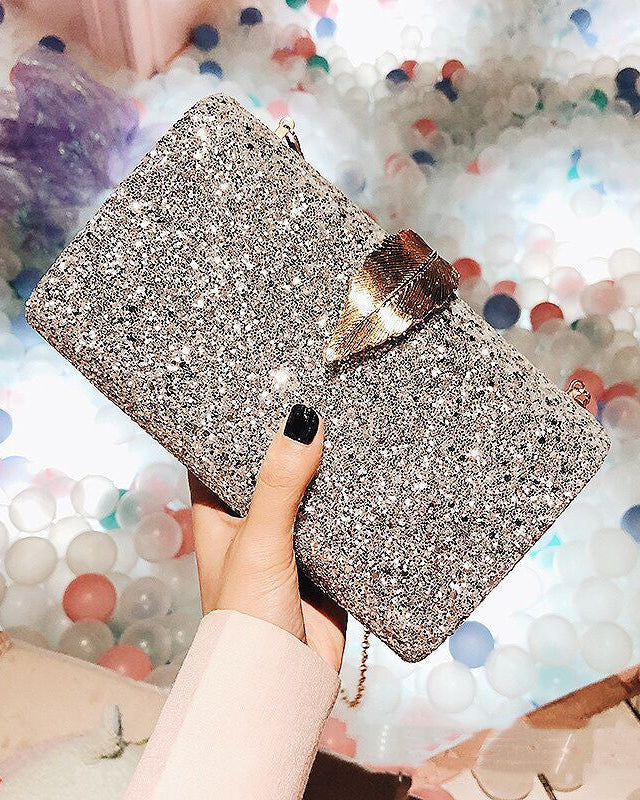 Silver glittery clutch held by a hand against a colorful confetti background