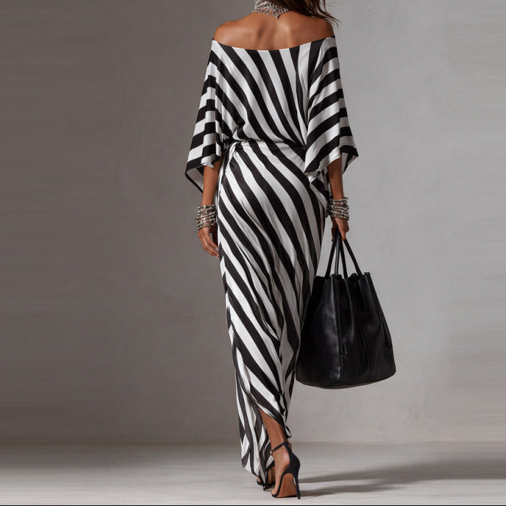 Woman wearing a black and white striped dress holding a black handbag against a gray background