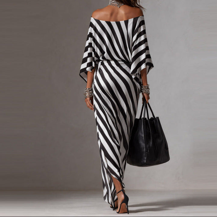 Woman wearing a black and white striped dress holding a black handbag against a gray background