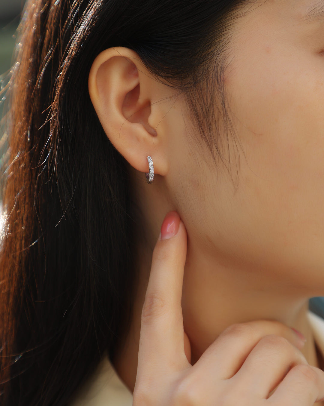 Close-up of an ear wearing a small hoop earring with a blurred background