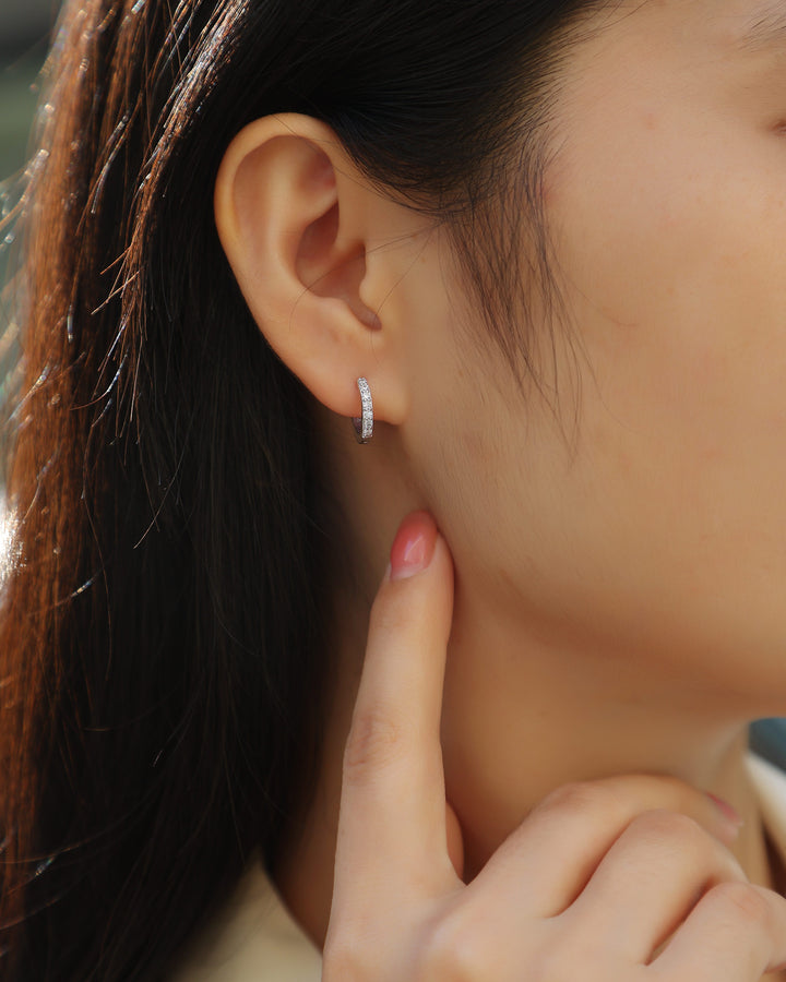 Close-up of an ear wearing a small hoop earring with a blurred background