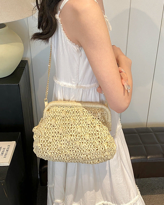 Woman holding a straw handbag in a room with a lamp and bookshelf.