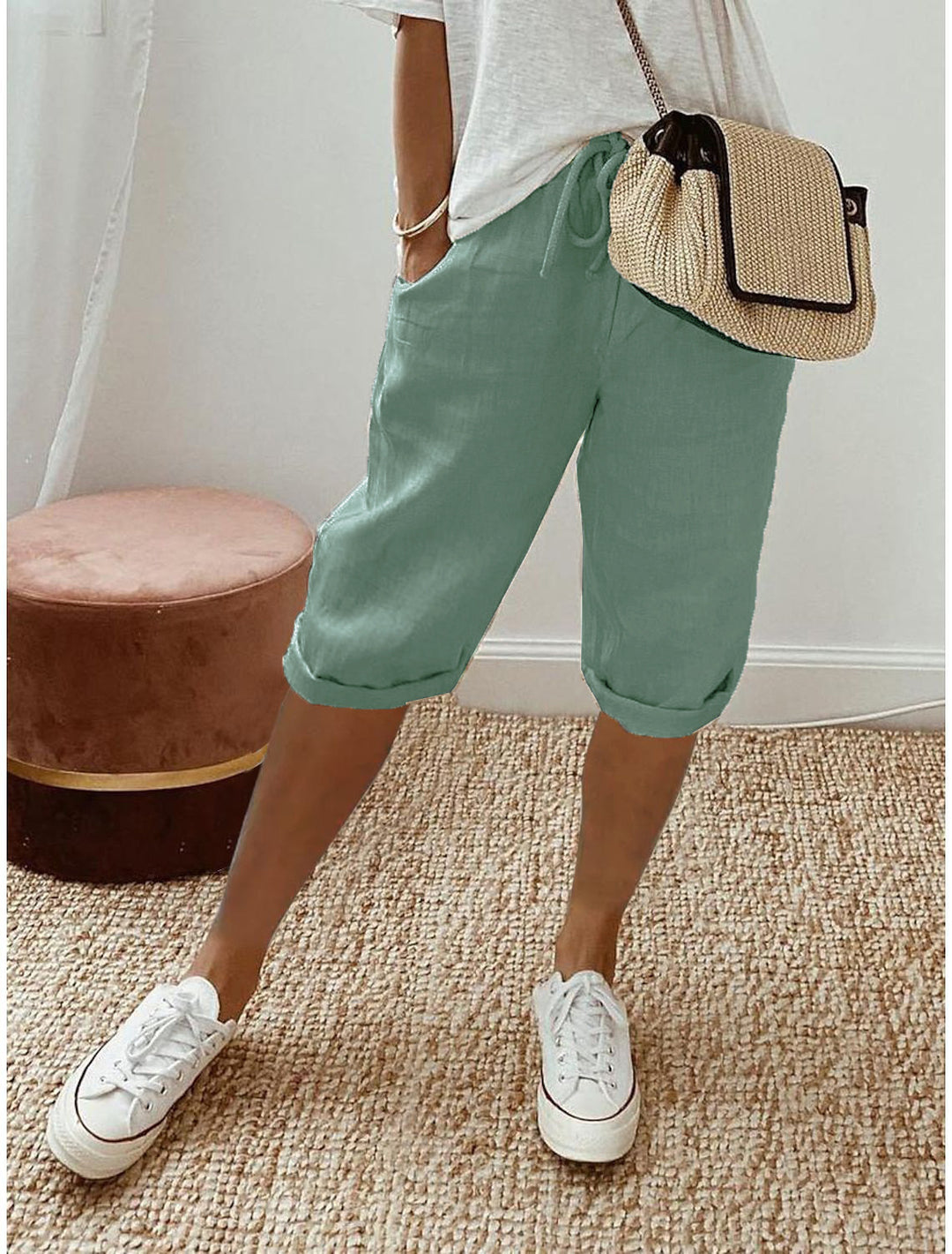 Person wearing green shorts, white sneakers, and a straw bag on a beige carpet.