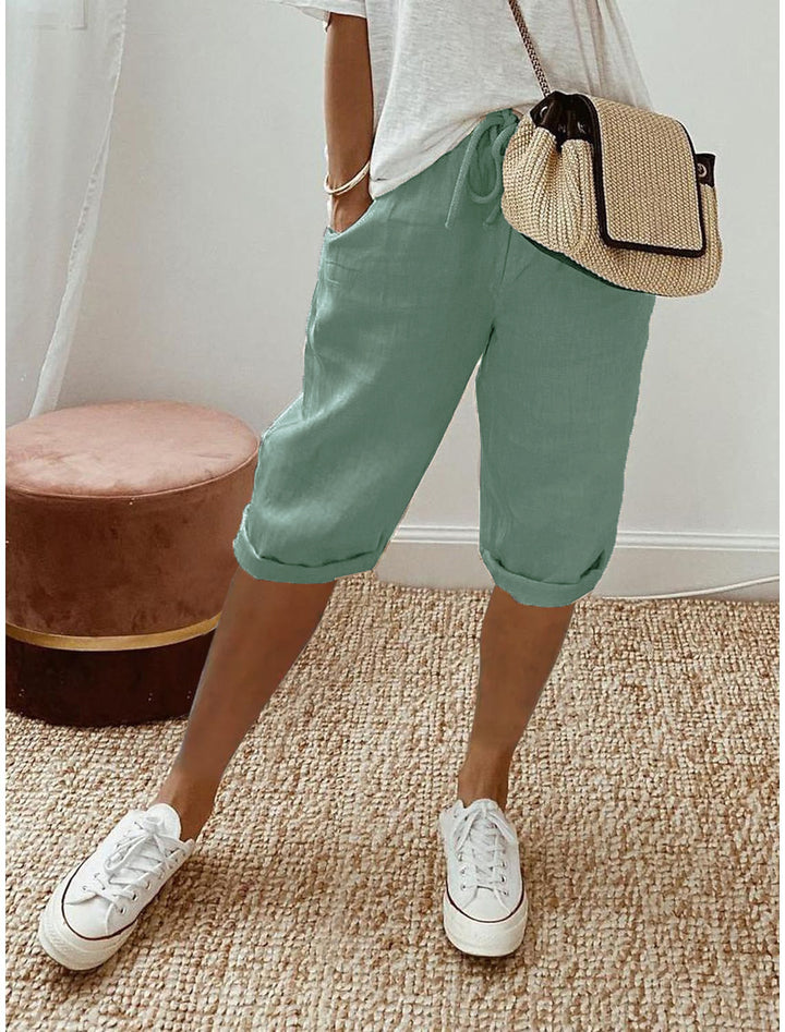 Person wearing green shorts, white sneakers, and a straw bag on a beige carpet.