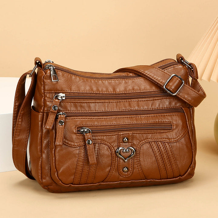 Brown leather handbag with multiple zippers on a beige background