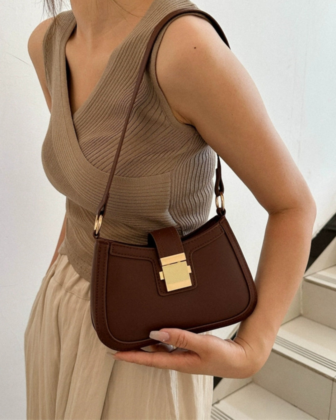 Woman holding a brown handbag with a gold clasp against a neutral background