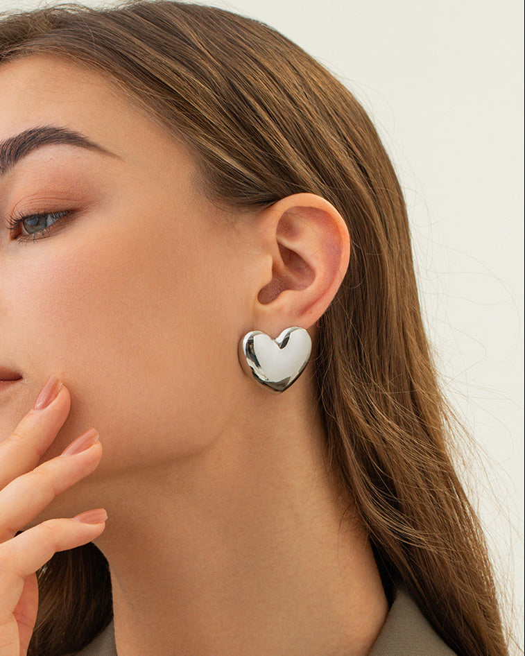 Woman wearing silver heart-shaped earrings with a neutral background