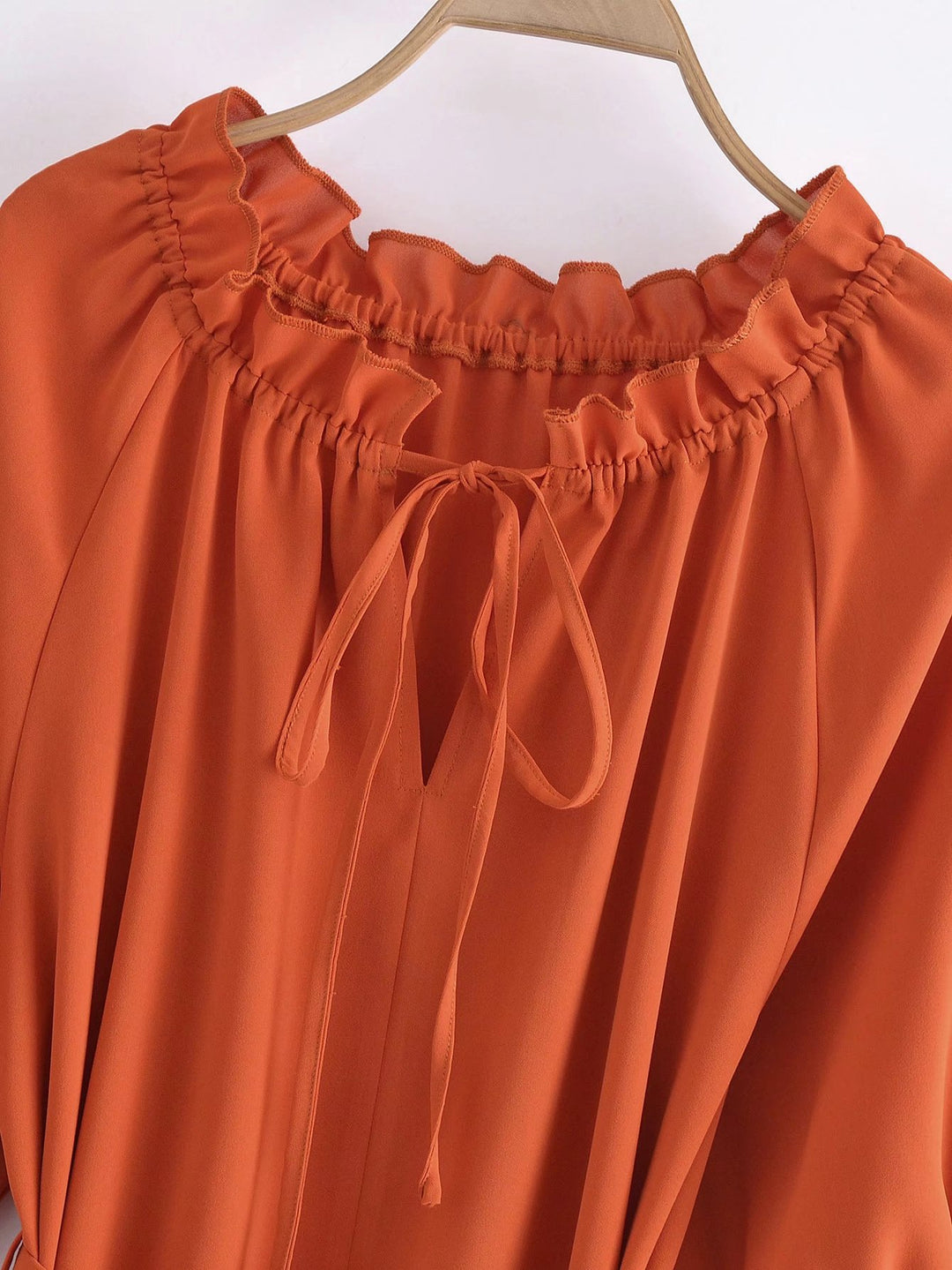 Orange blouse with long sleeves and tie details on a white background
