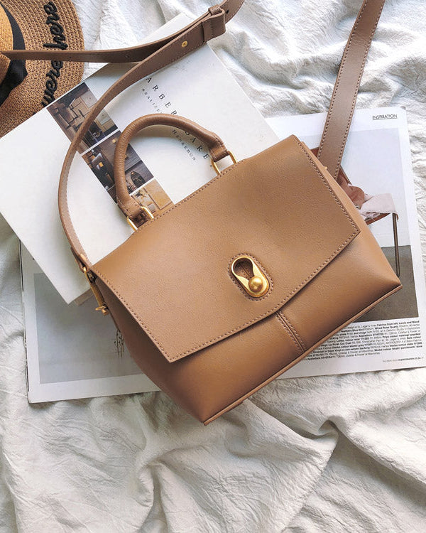Brown handbag on a magazine with a straw hat on a light fabric background