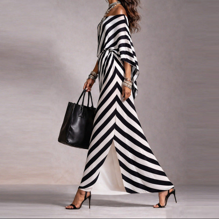 Woman wearing a black and white striped dress holding a black handbag against a gray background