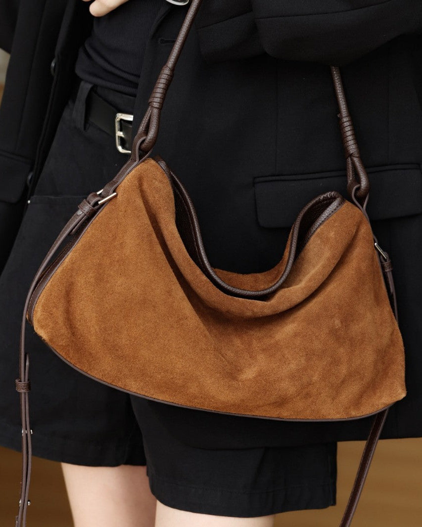 Brown suede handbag held by a person wearing a black outfit.
