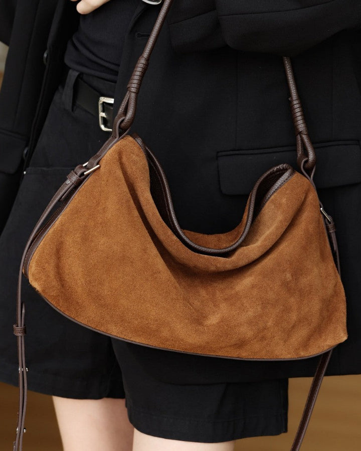 Brown suede handbag held by a person wearing a black outfit.