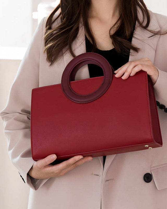 Person holding a red handbag with a unique handle design against a neutral background