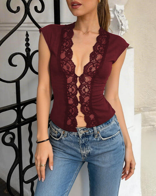 Woman wearing a burgundy lace top and blue jeans standing in front of an ornate black metal gate.