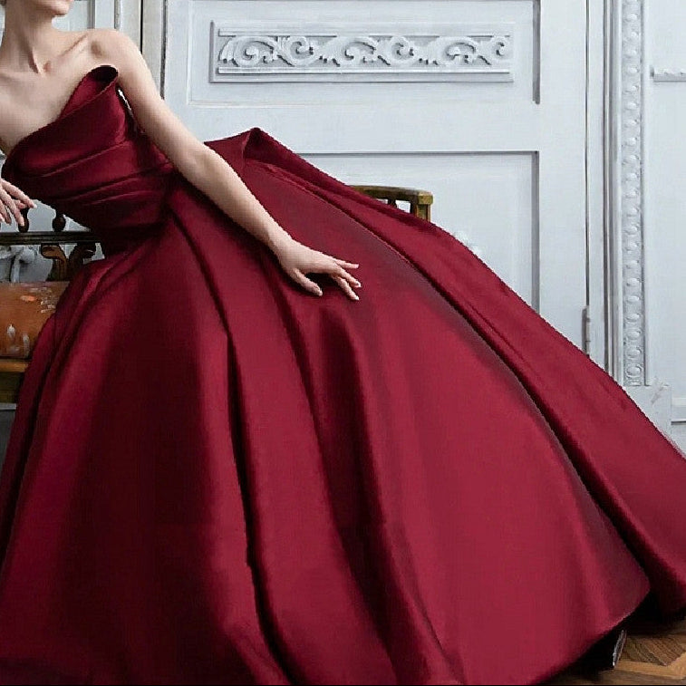 Woman in a burgundy gown sitting on a chair in an elegant room.