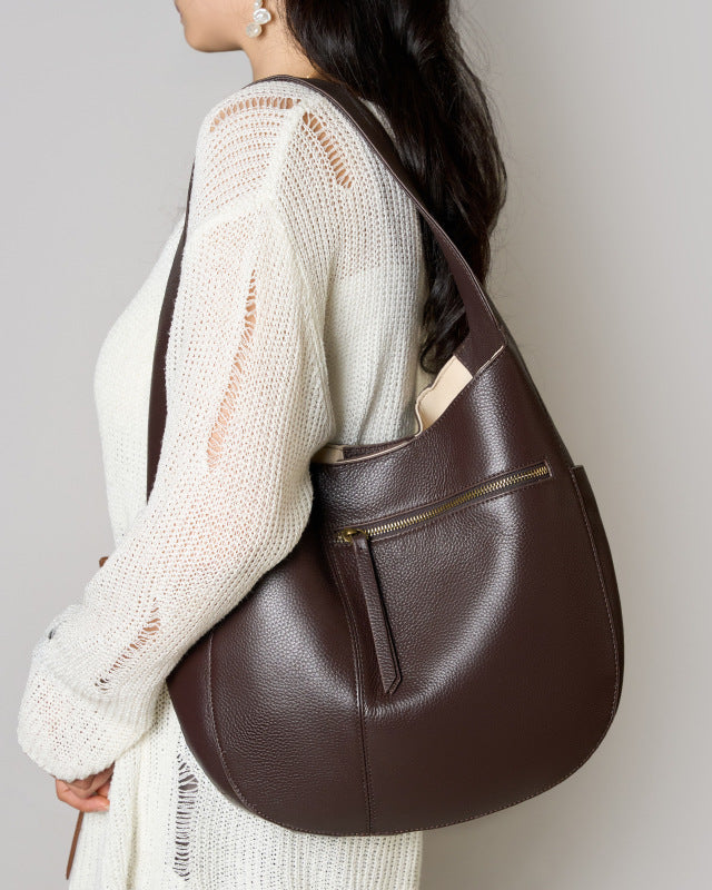 Person wearing a brown leather shoulder bag against a plain background
