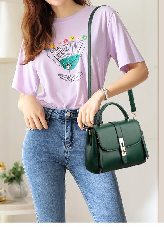 Woman wearing a light purple t-shirt with a colorful design, blue jeans, and holding a green handbag.