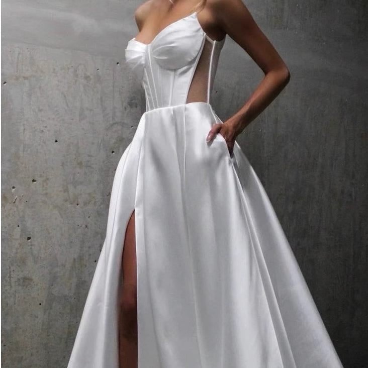 Woman wearing a white wedding dress with a high slit against a gray concrete wall.
