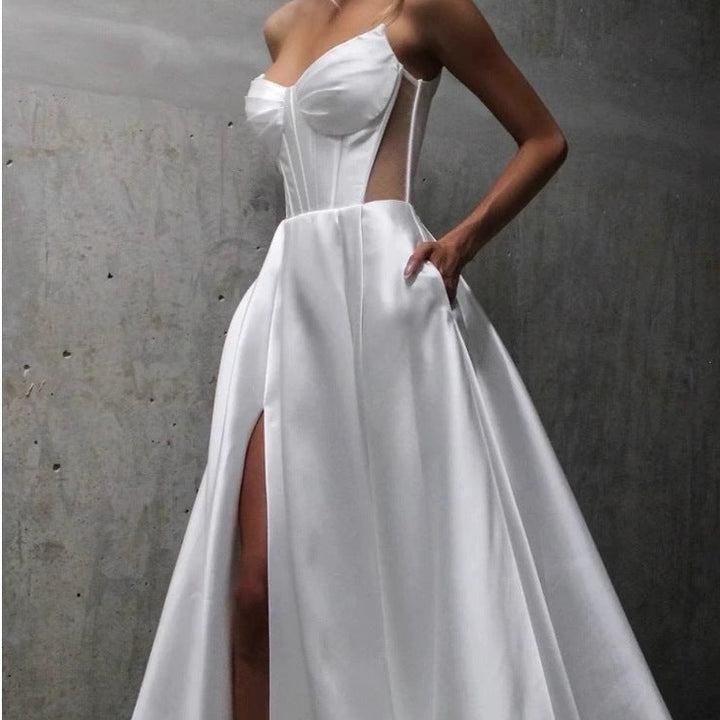 Woman wearing a white wedding dress with a high slit against a gray concrete wall.